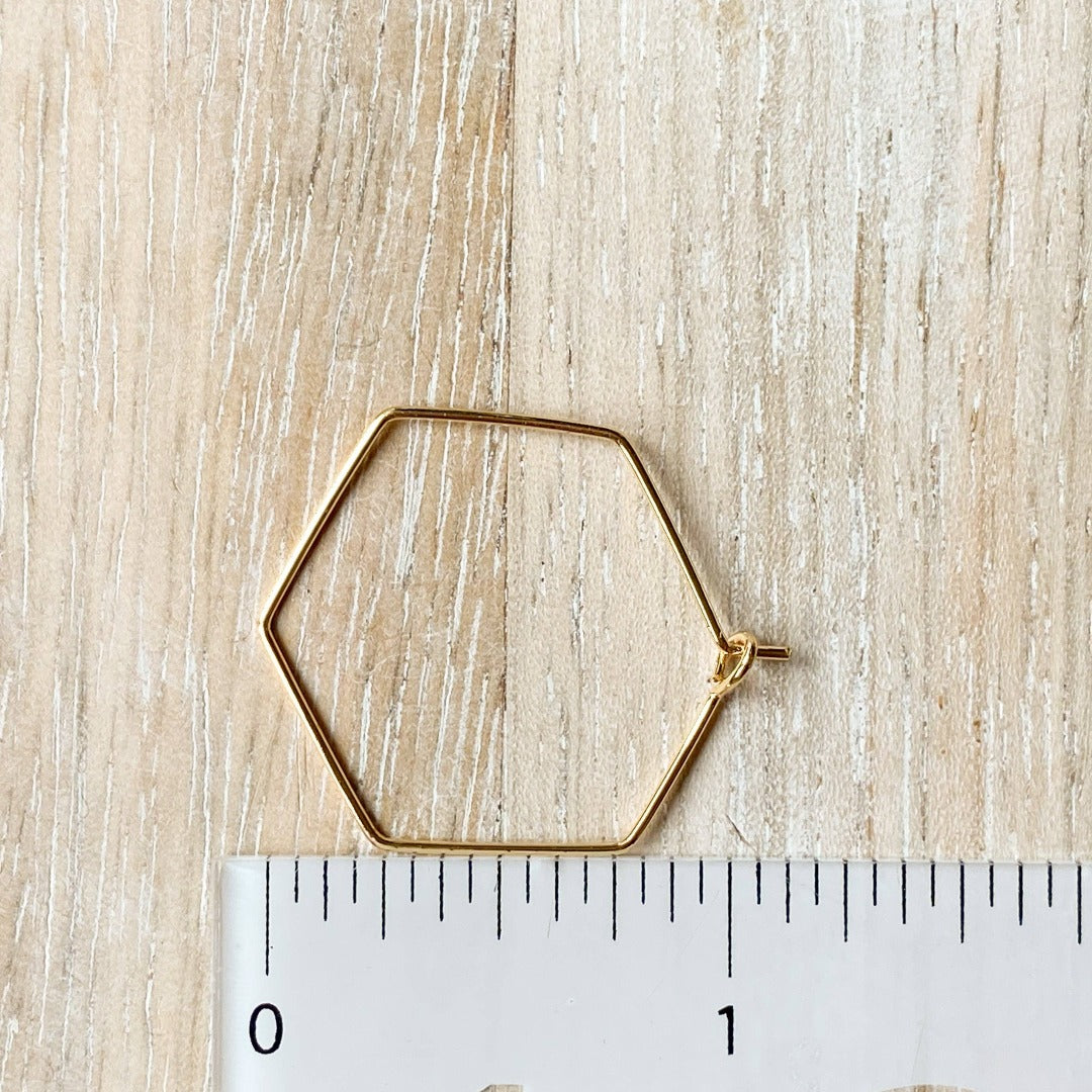 A pair of Agaveh Girl Gold Hexi Hoops, featuring a thin, gold wire hexagon design, displayed on a branded card with the text 'agaveh girl,' against a textured background with dried floral accents. The earrings are minimalist and geometric, available in Ottawa, Ontario, Canada.