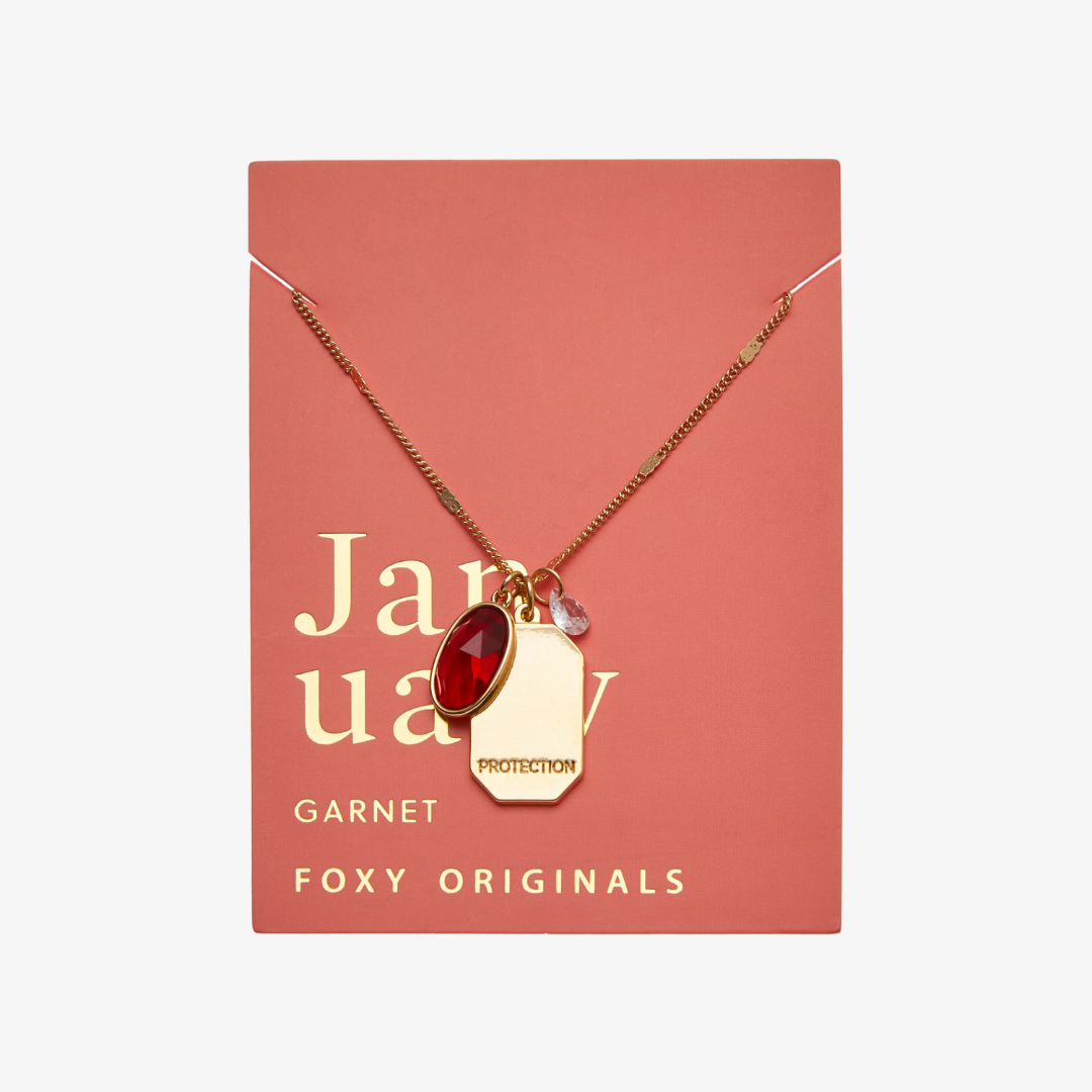 A collection of gold necklaces with colored gemstone pendants displayed on a light blue surface. Each pendant has a word engraved on it, such as "JOY," "FRIENDSHIP," "WISDOM," "HEALING," and "PROTECTION." The necklaces are arranged in a semicircle, with the pendants facing the viewer.