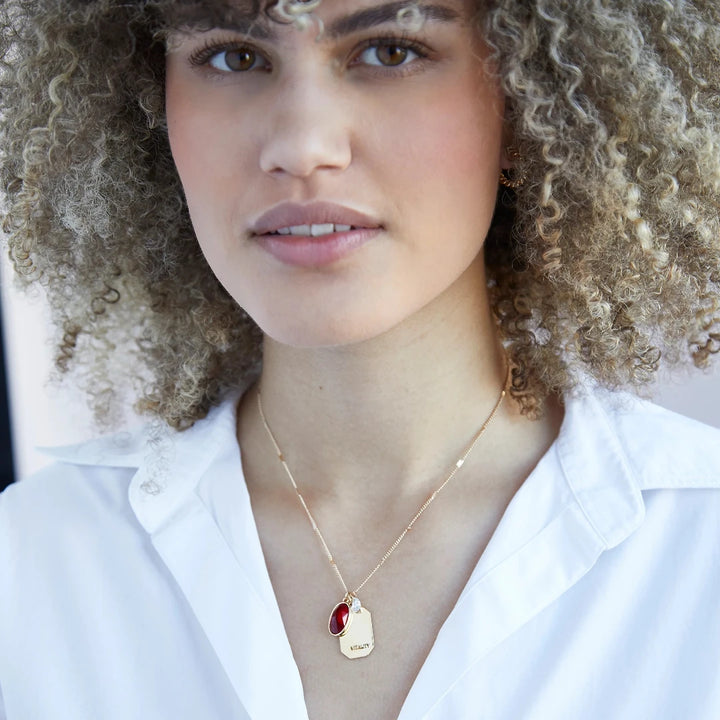 A gold necklace with a ruby stone pendant. The pendant also has the word 