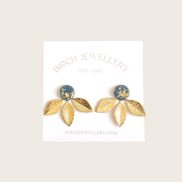 A pair of gold earrings with a leaf design. The earrings have a blue, circular resin center with gold flecks. The leaves are attached to the center and can be detached.