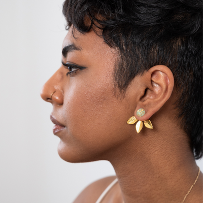A pair of gold earrings with a leaf design. The earrings have a green, circular resin center with gold flecks. The leaves are attached to the center and can be detached.