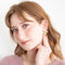 A pair of gold earrings with a leaf design. The earrings have a white, circular resin center with gold flecks. The leaves are attached to the center and can be detached.