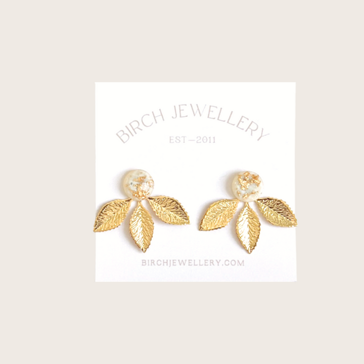 A pair of gold earrings with a leaf design. The earrings have a white, circular resin center with gold flecks. The leaves are attached to the center and can be detached.