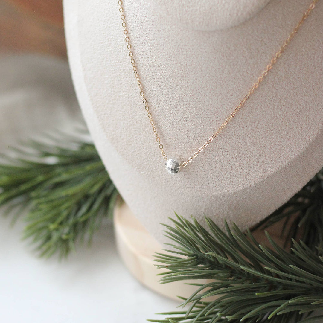 Gold necklace with a small silver bead on a mannequin bust with greenery in the background
