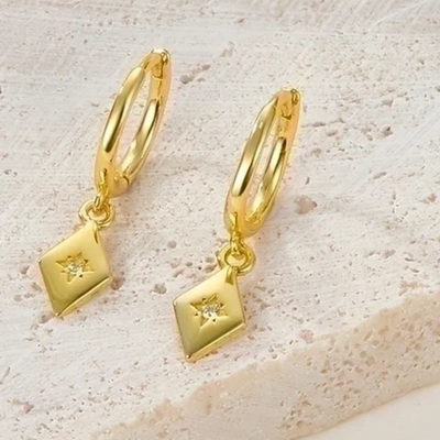 Gold plated diamond drop earrings featuring small gold hoops with dangling rhombus-shaped charms, each with a central sparkling crystal resembling a North Star. These elegant earrings are available in Ottawa, Ontario, Canada.