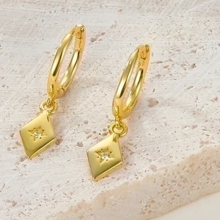 Gold plated diamond drop earrings featuring small gold hoops with dangling rhombus-shaped charms, each with a central sparkling crystal resembling a North Star. These elegant earrings are available in Ottawa, Ontario, Canada.