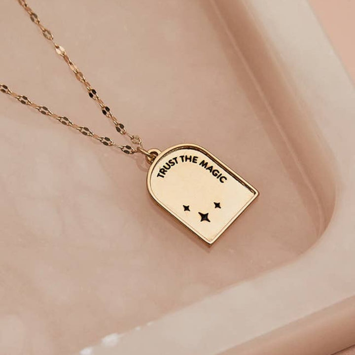 A gold necklace with a pendant shaped like an archway. The pendant has the words 
