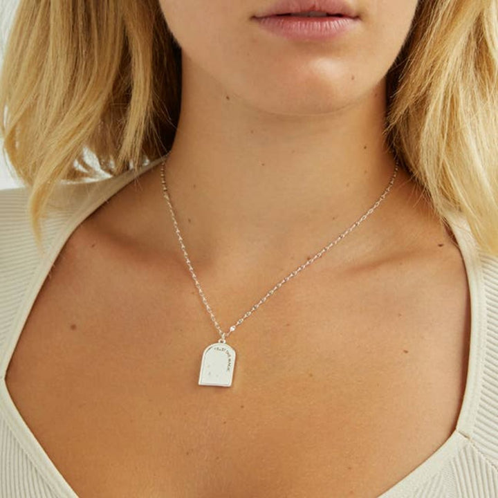 A silver necklace with a pendant shaped like an archway. The pendant has the words 