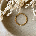 A gold twisted ring, featuring a woven or rope-like texture, displayed on a speckled ceramic dish with dried floral accents. The ring is dainty and stackable, available in Ottawa, Ontario, Canada.