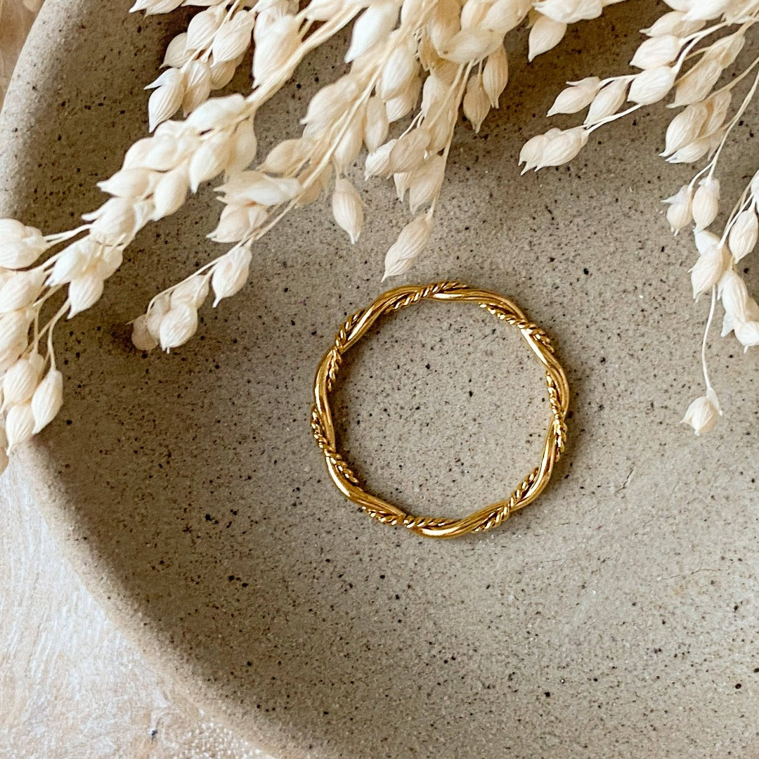 A gold twisted ring, featuring a woven or rope-like texture, displayed on a speckled ceramic dish with dried floral accents. The ring is dainty and stackable, available in Ottawa, Ontario, Canada.