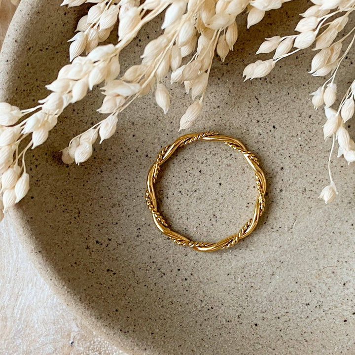 A gold twisted ring, featuring a woven or rope-like texture, displayed on a speckled ceramic dish with dried floral accents. The ring is dainty and stackable, available in Ottawa, Ontario, Canada.