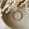 A gold twisted ring, featuring a woven or rope-like texture, displayed on a speckled ceramic dish with dried floral accents. The ring is dainty and stackable, available in Ottawa, Ontario, Canada.