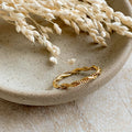 A gold twisted ring, featuring a woven or rope-like texture, displayed on a speckled ceramic dish with dried floral accents. The ring is dainty and stackable, available in Ottawa, Ontario, Canada.