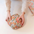 Person holding a round, floral-patterned product on a light background