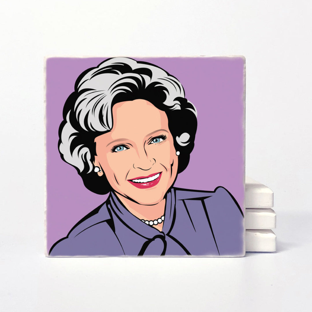 A square ceramic coaster featuring a stylized pop-art portrait of a smiling woman with short gray hair, blue eyes, and red lips, set against a lavender background. The coaster is displayed upright on a white surface with a stack of similar coasters behind it.