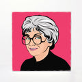 A square art print featuring a stylized pop-art portrait of a woman with short gray hair, round black glasses, and a black top against a bright pink background, shown on a light gray surface.