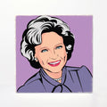 A square art print or card featuring a stylized pop-art portrait of a smiling woman with short gray hair, blue eyes, and a purple top against a lavender background, shown on a white surface.
