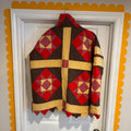 Quilt with red and brown geometric pattern draped over a white door with yellow trim.