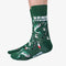 A pair of green crew socks featuring a fishing-themed pattern with illustrations of leaping fish, fishing rods, bobbers, and lures in shades of white, red, and black. One sock displays the text 