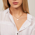 Woman wearing a gold necklace with a heart pendant against a neutral background