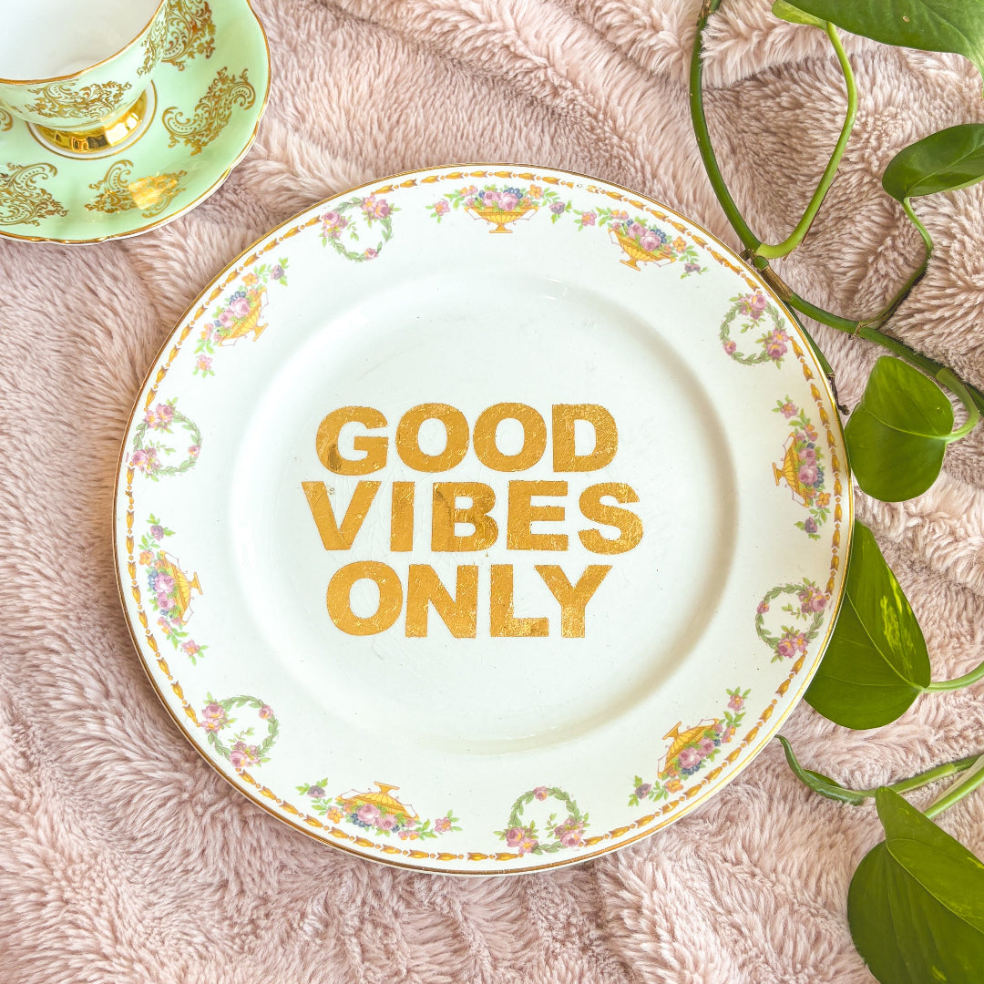 Decorative plate with 'Good Vibes Only' text on a textured surface with leaves.