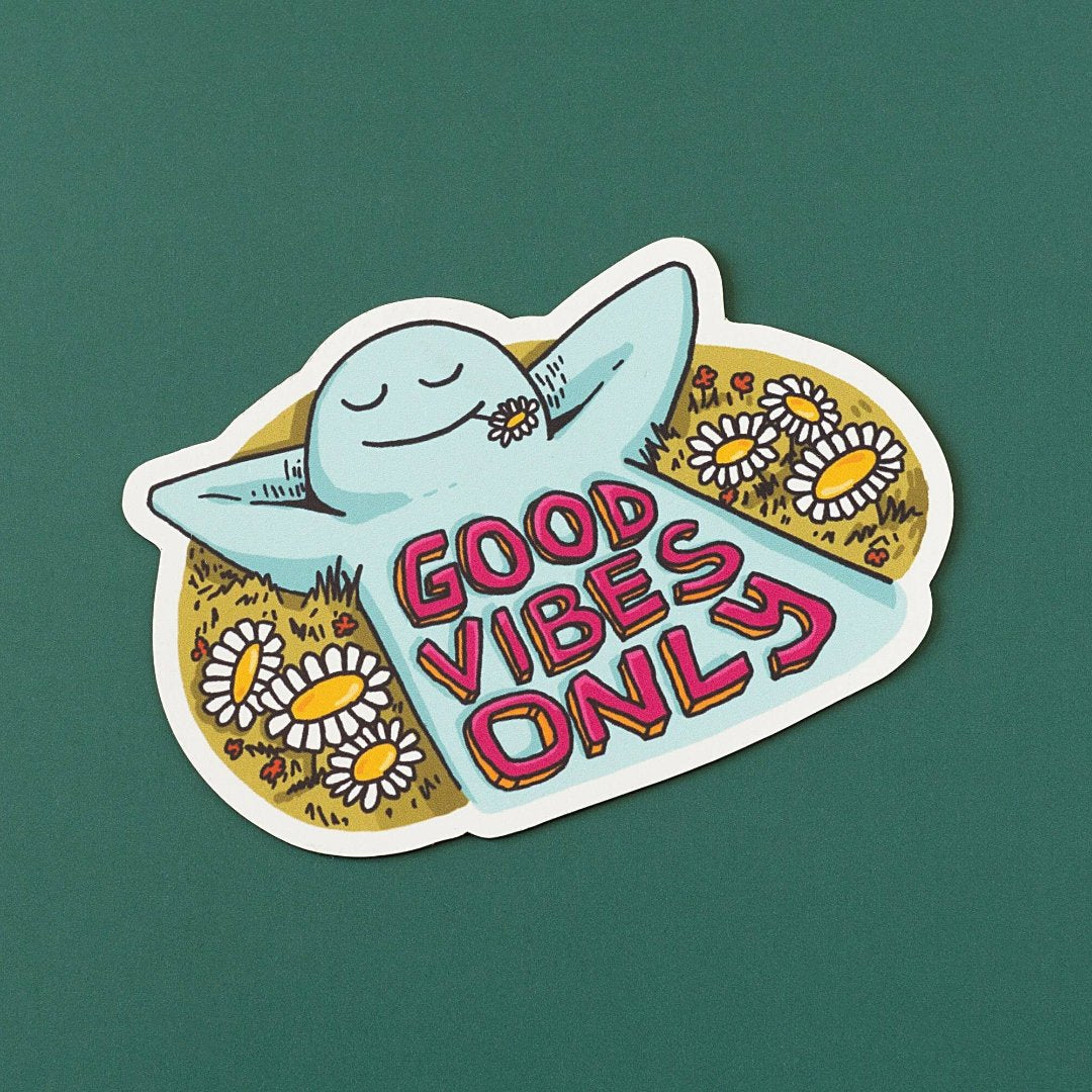 A blue, cartoon character with arms outstretched is lying on its back in a field of daisies. The text "GOOD VIBES ONLY" appears in bold, colorful letters below the character.