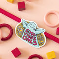 A blue, cartoon character with arms outstretched is lying on its back in a field of daisies. The text "GOOD VIBES ONLY" appears in bold, colorful letters below the character.