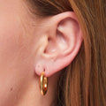 Gold hoop earring worn by a person with brown hair.