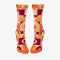 A pair of women's crew socks with a bold, abstract pattern in shades of orange, yellow, pink, and purple. Text on one sock reads 