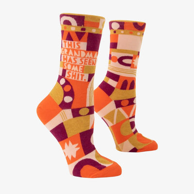 A pair of women's crew socks with a bold, abstract pattern in shades of orange, yellow, pink, and purple. Text on one sock reads 
