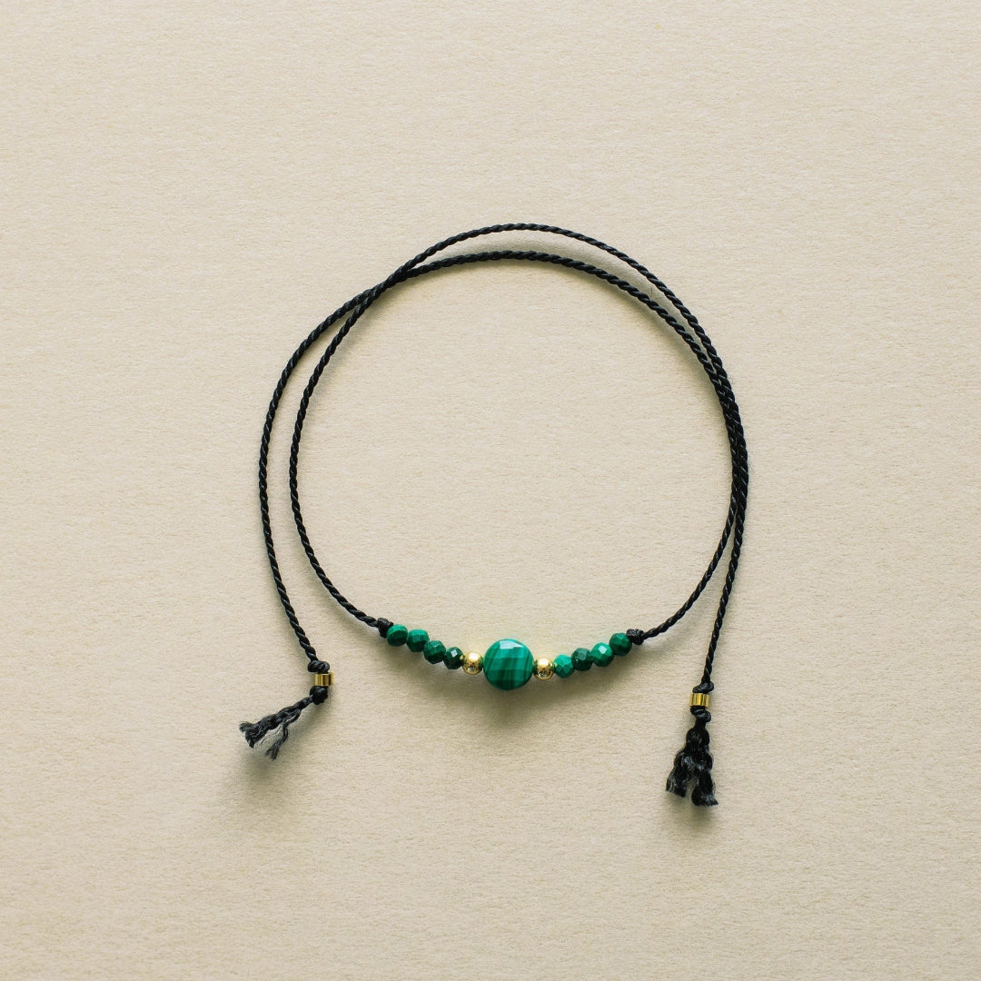 Necklace with black cord and green beads on a beige background