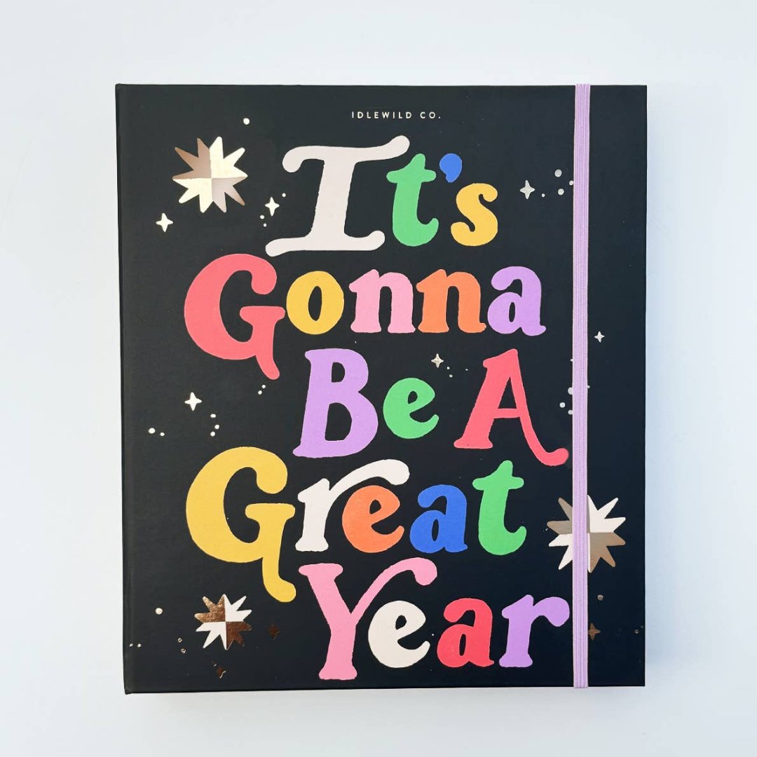 A black agenda with the phrase "It's Gonna Be A Great Year" written in colorful letters. The letters are outlined in gold and there are gold stars scattered around the text. The agenda has a purple elastic band.