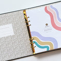 A black agenda with the phrase "It's Gonna Be A Great Year" written in colorful letters. The letters are outlined in gold and there are gold stars scattered around the text. The agenda has a purple elastic band.