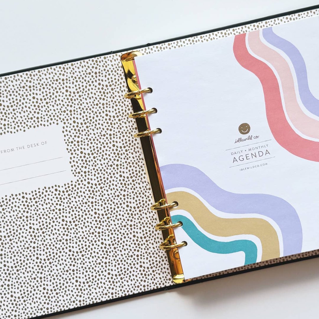 A black agenda with the phrase "It's Gonna Be A Great Year" written in colorful letters. The letters are outlined in gold and there are gold stars scattered around the text. The agenda has a purple elastic band.