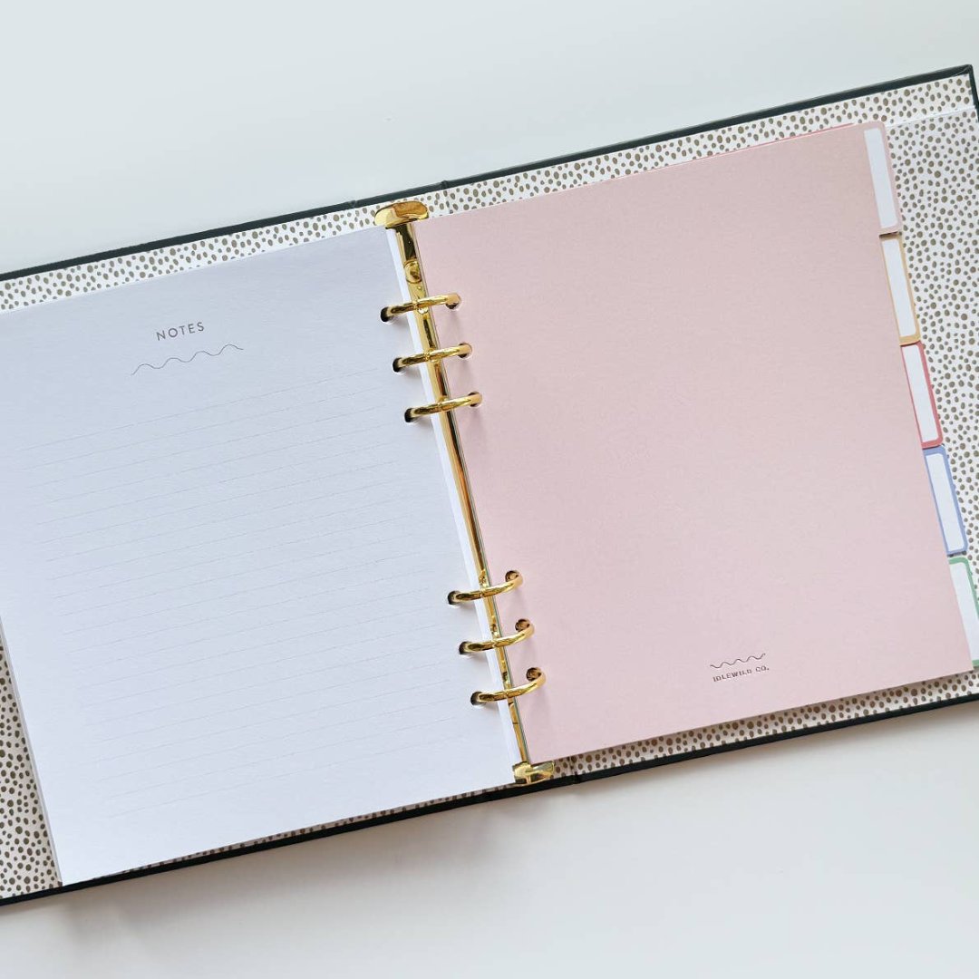 A black agenda with the phrase "It's Gonna Be A Great Year" written in colorful letters. The letters are outlined in gold and there are gold stars scattered around the text. The agenda has a purple elastic band.