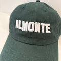 A dark green baseball cap with 'ALMONTE' embroidered in white block letters across the front, shown against a plain light background.