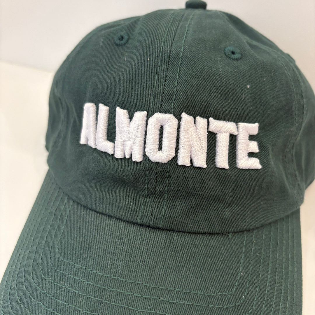 A dark green baseball cap with 'ALMONTE' embroidered in white block letters across the front, shown against a plain light background.