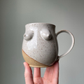 White Speckled Boob Mug, a ceramic coffee cup with two breasts on the front in the colour white with a speckled texture, and a angled beige natural clay at the bottom.