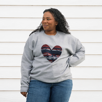 a grey sweatshirt with a large, heart-shaped patch. The patch features a Native American-inspired geometric pattern in shades of red, blue, and white.