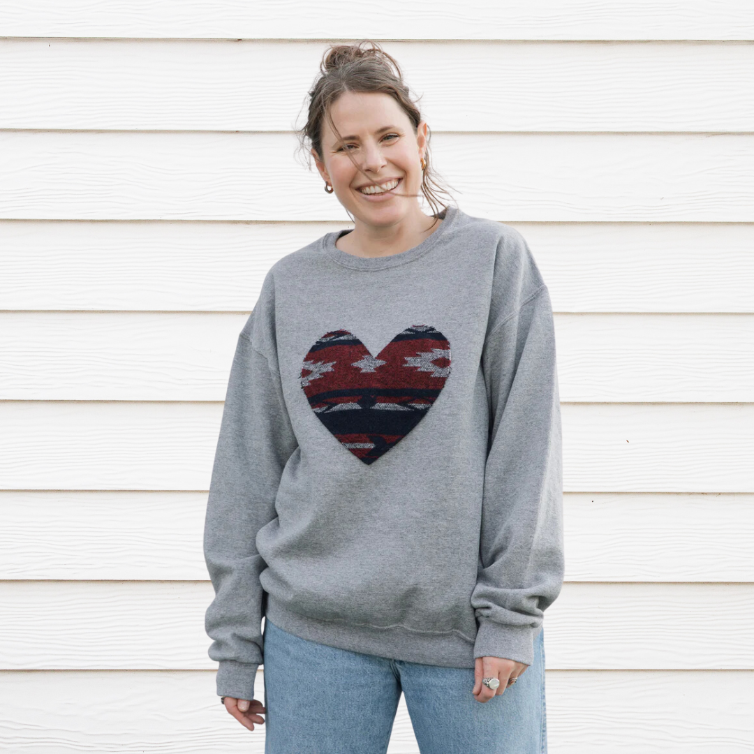 a grey sweatshirt with a large, heart-shaped patch. The patch features a Native American-inspired geometric pattern in shades of red, blue, and white.