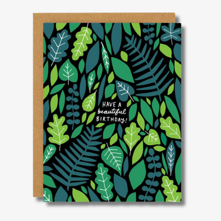 Colourful birthday card with a vibrant pattern of various green and blue leaves on a black background. In the center, white text reads 'Have a beautiful birthday!' The card is bordered by a kraft paper edge, adding a natural and earthy touch.