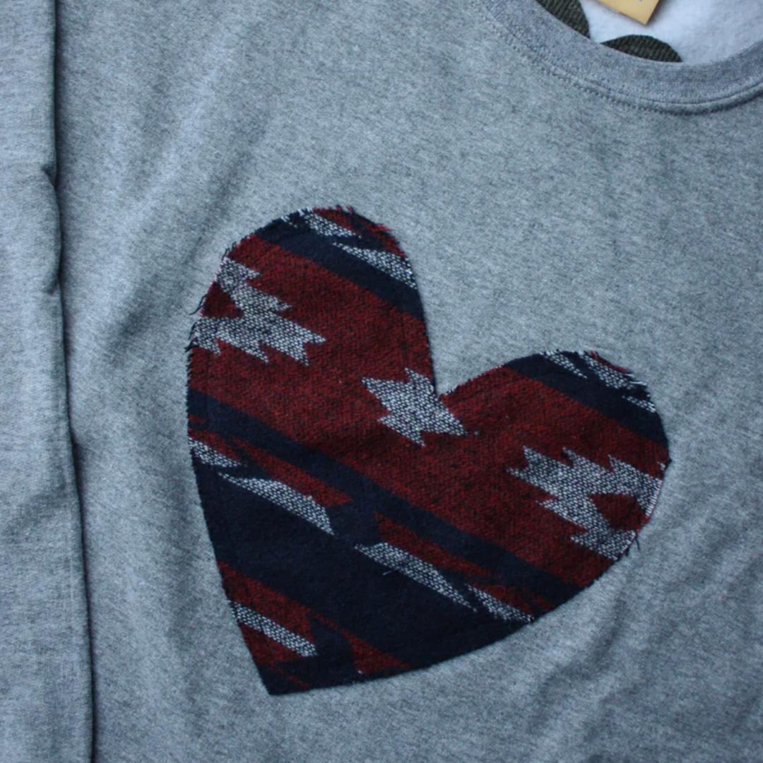 a grey sweatshirt with a large, heart-shaped patch. The patch features a Native American-inspired geometric pattern in shades of red, blue, and white.