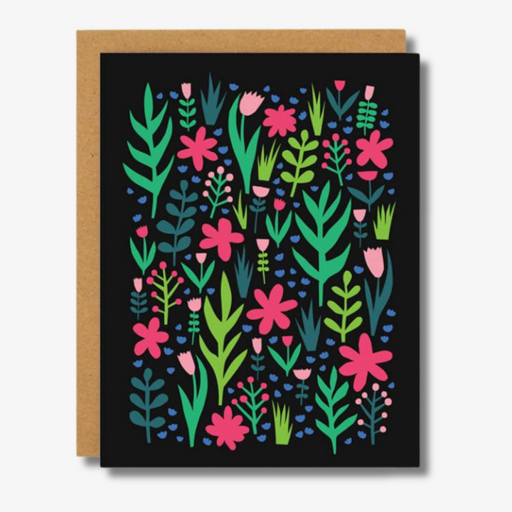 Bright and cheerful greeting card featuring a lively pattern of various pink, green, and blue flowers and leaves against a black background. The card is accompanied by a kraft paper envelope in the background, adding a rustic and natural touch.