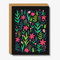 Bright and cheerful greeting card featuring a lively pattern of various pink, green, and blue flowers and leaves against a black background. The card is accompanied by a kraft paper envelope in the background, adding a rustic and natural touch.