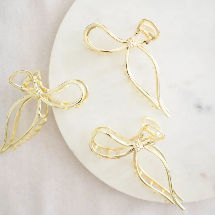 Gold Metallic Bow Clip, a claw clip in a gold metallic finish. Perfect for adding a feminine touch to any hairstyle.