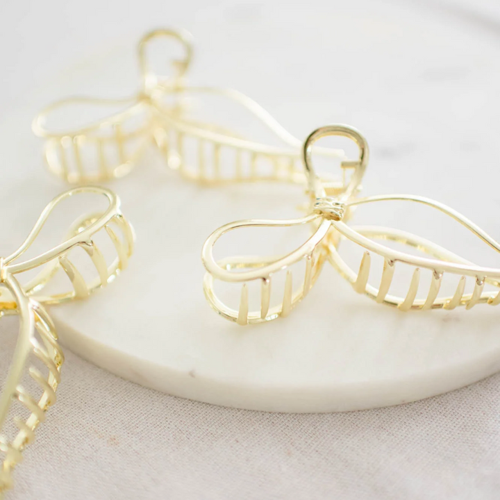 Gold Metallic Bow Clip, a claw clip in a gold metallic finish. Perfect for adding a feminine touch to any hairstyle.