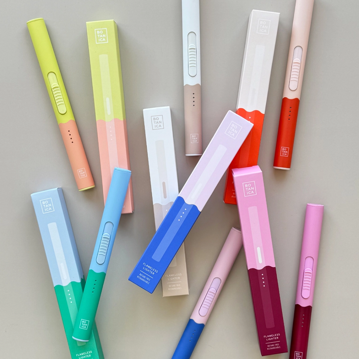 6 DuoTone Flameless Lighter in different colour combinations that include, pink and berry, white and beige, blue and green, yellow and peach, pink and blue, and peach and orange piled with their boxes.