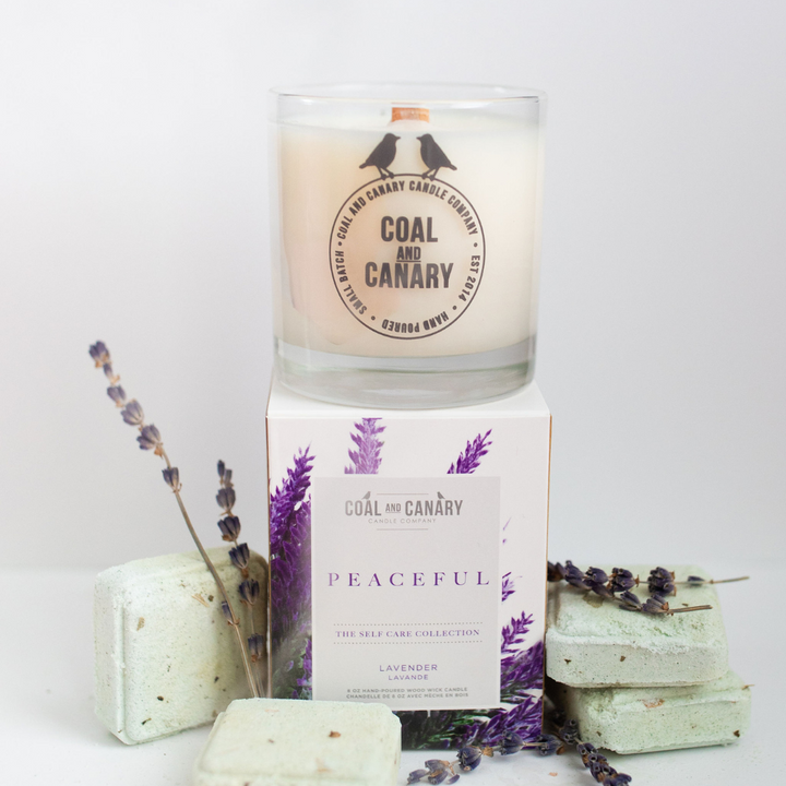 Peaceful Candle, a glass jar candle on its box surrounded by lavender and bath soaks.