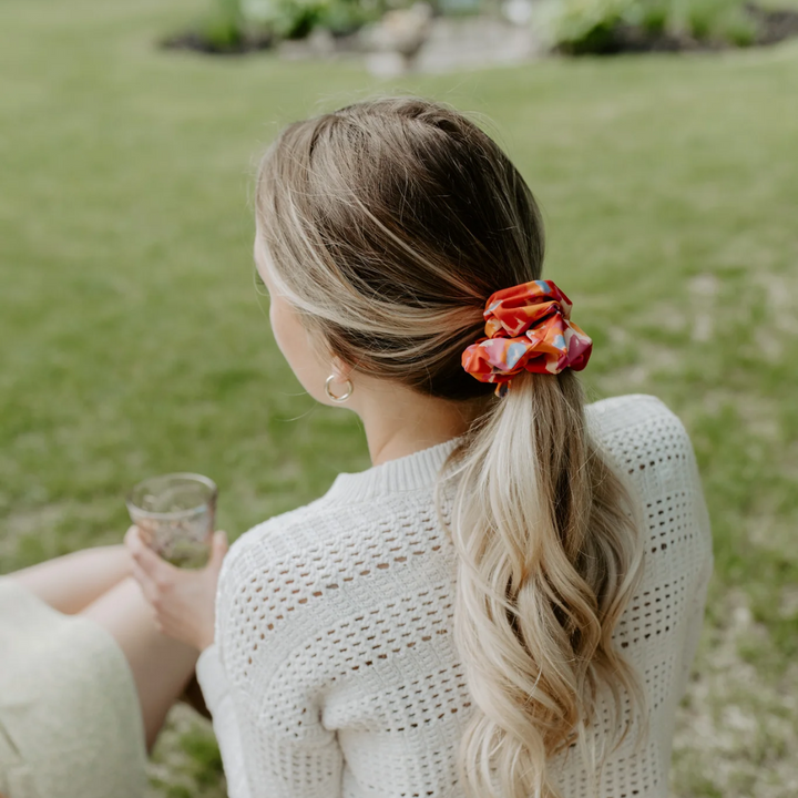 Flower Child Petite Scunchie, a fluffy hair tie in a rainbow of tiedye colours in a blonde woman's hair.