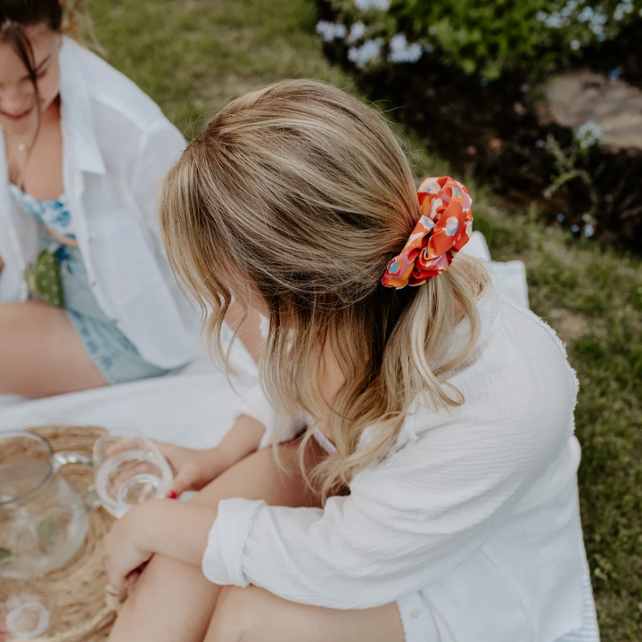 Flower Child Petite Scunchie, a fluffy hair tie in a rainbow of tiedye colours in a blonde woman's hair.